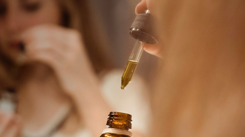 A woman standing in front of a bathroom mirror taking cbd from a glass dropper