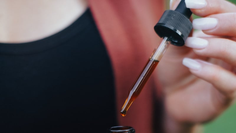 A woman holding a glass CBD oil dropper 