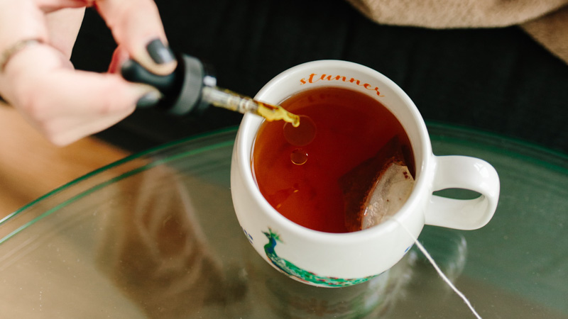 Woman dropping CBD oil into a cup of tea
