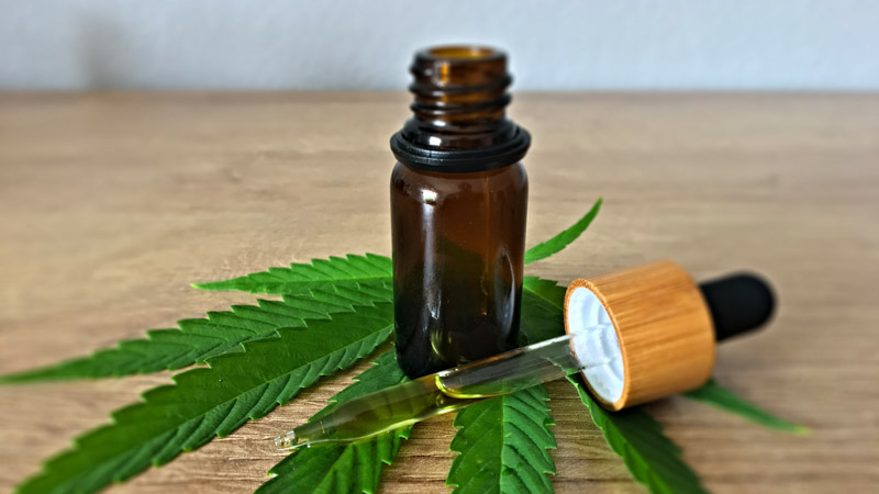 CBD oil dropper and bottle on top of a hemp leaf on a wooden table