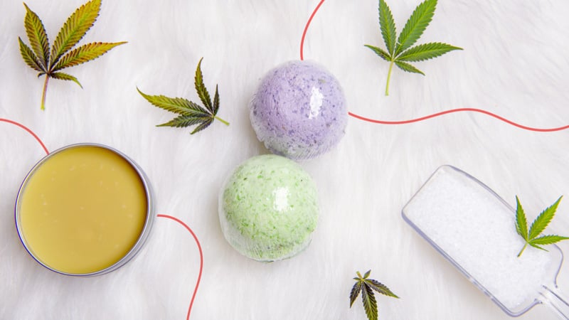 CBD bath bomb and CBD topicals on marble floor with hemp leaves