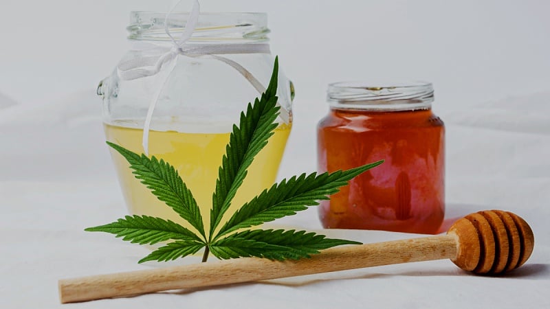 Bottle of CBD oil with a cannabis leaf and a bottle of honey