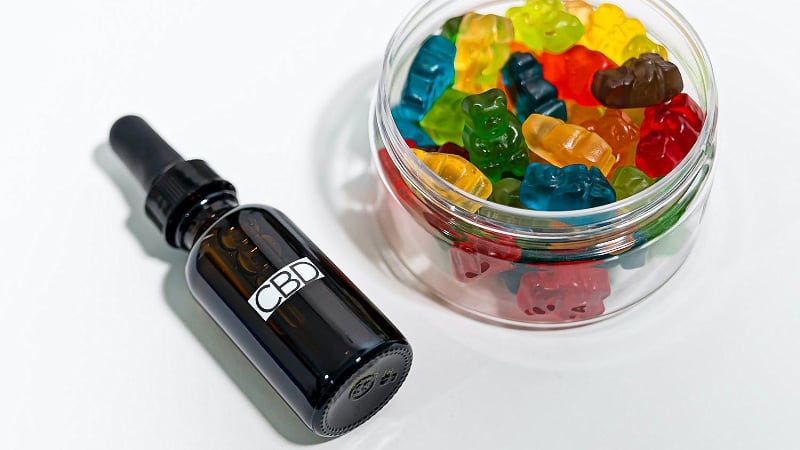 a bottle of CBD oil and a container with hemp gummies on a white background