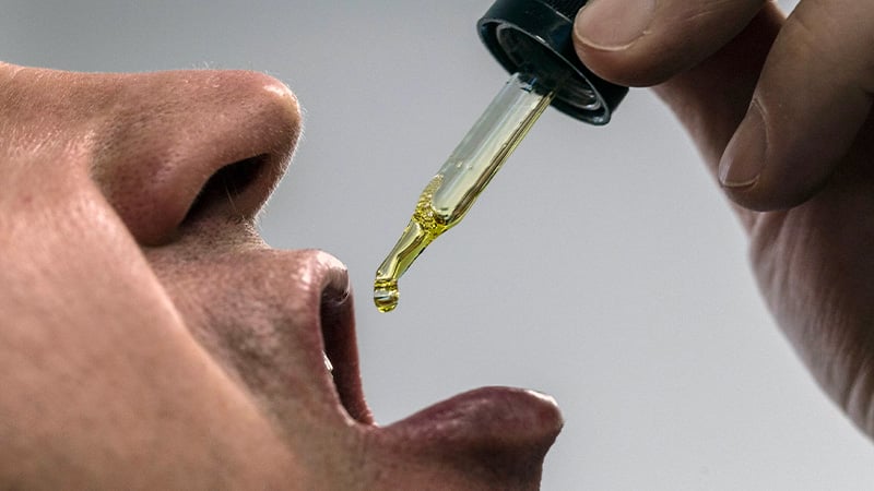 A man taking CBD oil, dropping it to his mouth.